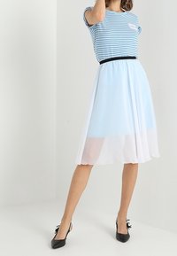 Raidallinen sininen toppi lyhyillä hihoilla, musta vyö vyötäröllä ja valuva vaaleansininen ja valkoinen hame, jota täydentävät mustat korkokengät.