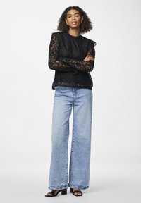 Svart blonde topp med lange ermer, skjært halslinje og hem, kombinert med vide lyseblå jeans og svarte blokkhevede sandaler.