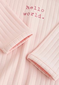 Rosa geripptes Stoffmaterial mit umgeschlagenen Ärmeln und dem in roter Kleinbuchstaben-Schreibmaschinenschrift gedruckten Text "hello world." auf der Vorderseite.