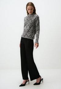 Grau und schwarz gestreifter Pullover mit einem gerippten Halsausschnitt, kombiniert mit schwarzen weit geschnittenen Hosen und schwarzen High-Heels.