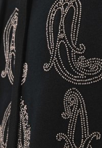 Czarna tkanina z misternymi, srebrnymi aplikacjami z koralików tworzącymi płynny wzór. Tekstura wydaje się gładka, z delikatnym połyskiem koralików.