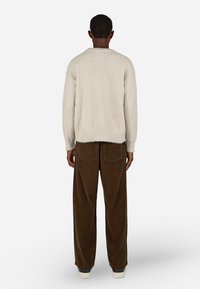 Suéter bege texturizado com um corte relaxado, combinado com calças de veludo cotelê castanhas de perna larga. Design simplista e palete de cores neutras.