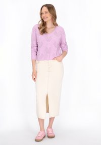 Maglione di lavanda lavorato a maglia con motivi testurizzati, abbinato a una gonna midi di jeans color crema con uno spacco frontale e sneakers rosa.