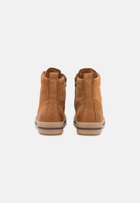 Beżowe zamszowe botki do kostki o gładkim wykończeniu, lekko zaokrąglonym nosku, bocznych zamkach błyskawicznych oraz tanowych gumowych podeszwach z subtelnym wzorem pasków.
