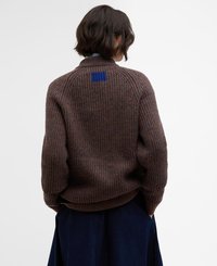 Pull en maille côtelée marron avec un col montant, présentant un accent carré bleu à l'arrière, porté sur une jupe bleu marine. Matière en tricot texturé.