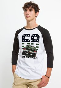 Raglan baseball t-shirt med hvid krop og sorte ærmer. Har et grafik af en grøn fastback-bil, "68", og tekst nedenunder i fed sort.