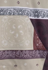 Bavlněná látka s béžovým pozadím a burgundskými a černými paisley vzory. Zahrnuje složité květinové a paisley motivy.