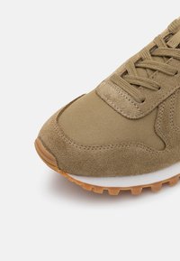 Avant de sneaker marron clair avec suède texturé et matériaux en tissu, lacets assortis, semelle intermédiaire blanche et semelle extérieure en caoutchouc naturel.