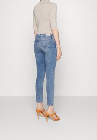 Vaqueros ajustados de mezclilla de color azul claro con cinco bolsillos y costuras sutiles. Combinados con sandalias de tacón alto con tiras naranjas.