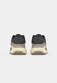 Un paio di scarpe da corsa Nike nere e grigie visto da dietro con soletta di colore crema e dettagli a motivo sul tallone.