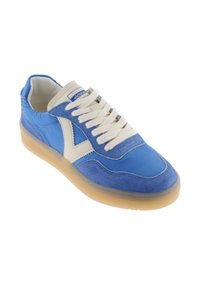 Zapatilla azul con cordones y logo blancos, suela beige y detalles en ante, presentada en ángulo para mostrar el lado exterior y la vista superior.