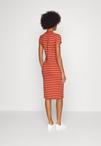 Paskowana sukienka midi w kolorach czerwonym, pomarańczowym i kremowym; dopasowany fason; krótkie rękawy; elastyczny materiał; połączona z białymi sneakersami.
