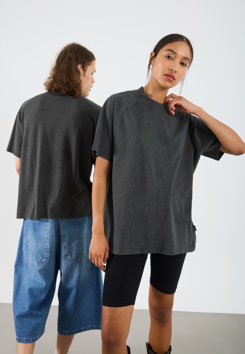 Mørkegrå oversized T-shirt med rund hals og korte ærmer, vist fra forsiden og bagsiden mod en neutral baggrund.