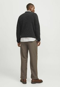 Pulover negru cu model în cleme, cu decolteu rotund, purtat deasupra unei cămăși albe cu dungi, combinat cu pantaloni bej și pantofi maro. Stil casual.