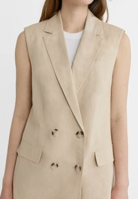 Beżowa, bezrękawnikowa, dwurzędowa kamizelka z lekkiego materiału. Posiada klapy z wycięciem, dwie przednie kieszenie oraz kontrastowe guziki.