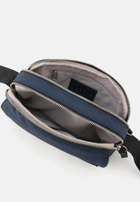 Navy Crossbody-Tasche mit zwei Reißverschlussfächern, glattem Äußeren, Stofffutter und verstellbarem Gurt. Das Innere umfasst eine Reißverschlusstasche.