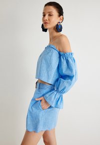 Top corto azul sin hombros con mangas abullonadas y patrón floral, combinado con una falda a juego con dobladillo ondulado y bolsillos.