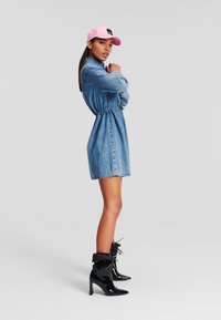 Denim obleka z nabiranjem na pasu, svetlo modre barve in kratke dolžine; v paru z sijočimi črnimi gležnjarji in roza kapo.