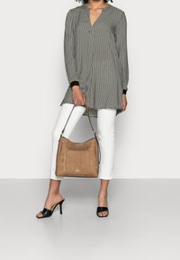 Tunique à motifs floraux en noir et blanc, associée à un jean blanc et des talons ouverts noirs. Sac à main en cuir souple marron clair avec une poche avant.