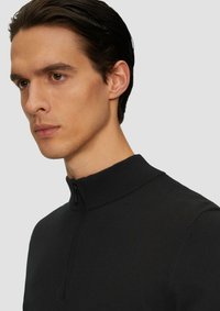 Czarny sweter z zamkiem na szyi, z prążkowanym kołnierzem i gładką teksturą. Dopasowany krój, minimalistyczny design podkreślający prostotę i wszechstronność.