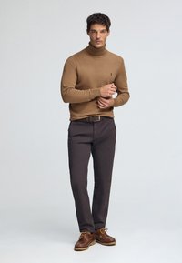 Brun polotröja och mörka byxor med bälte. Bruna skor med gula skosnören. Enkel design, slät textur. Neutralt bakgrund.