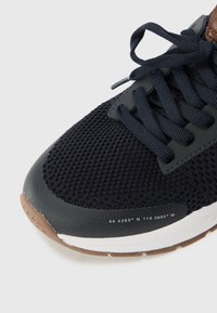 Black mesh sneaker featuring a textured upper, dark laces, and brown accents. Notable details include printed coordinates and a white midsole.
