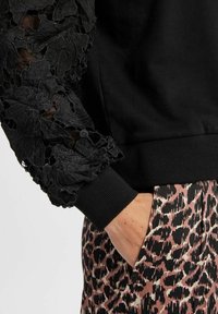 Felpa nera con maniche in pizzo testurizzato, caratterizzata da motivi floreali. I polsini sono a costine. Abbinata a pantaloni a fantasia rosa e nera.
