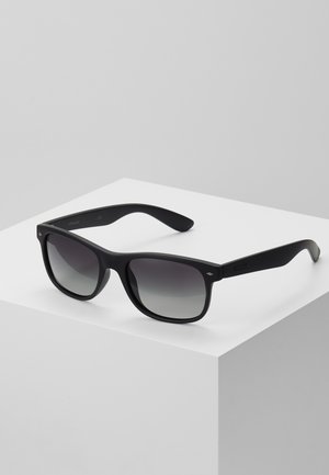 Lunettes de soleil noires avec une finition mate, de forme carrée, verres gris dégradés et logo subtil sur les branches. Texture non réfléchissante.