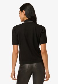 Schwarzer, kurzärmeliger Pullover mit Kragen und strukturiertem Finish, das einen subtilen Akzent am Kragen und eine taillierte Silhouette aufweist.