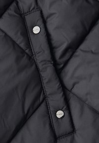 Musta tikattu kangas, jossa kaksi kiiltävää hopeanväristä painiketta pystysuorassa nauhassa toppatakin sulkemisessa.