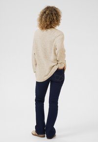 Beige striktrøje med en løs pasform, sænkede skuldre og ribbede manchetter, parret med mørkeblå flagrende jeans med design på baglommen.