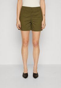 Shorts verde oliva con una cintura ajustada, bolsillos delanteros y un tejido ligero y suave. Combinados con tacones negros de punta afilada.