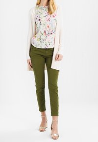 Blommig blus i pastellfärger, krämfärgad kofta, olivgröna byxor som sitter fint och ljusguldfärgade klacksandaler.