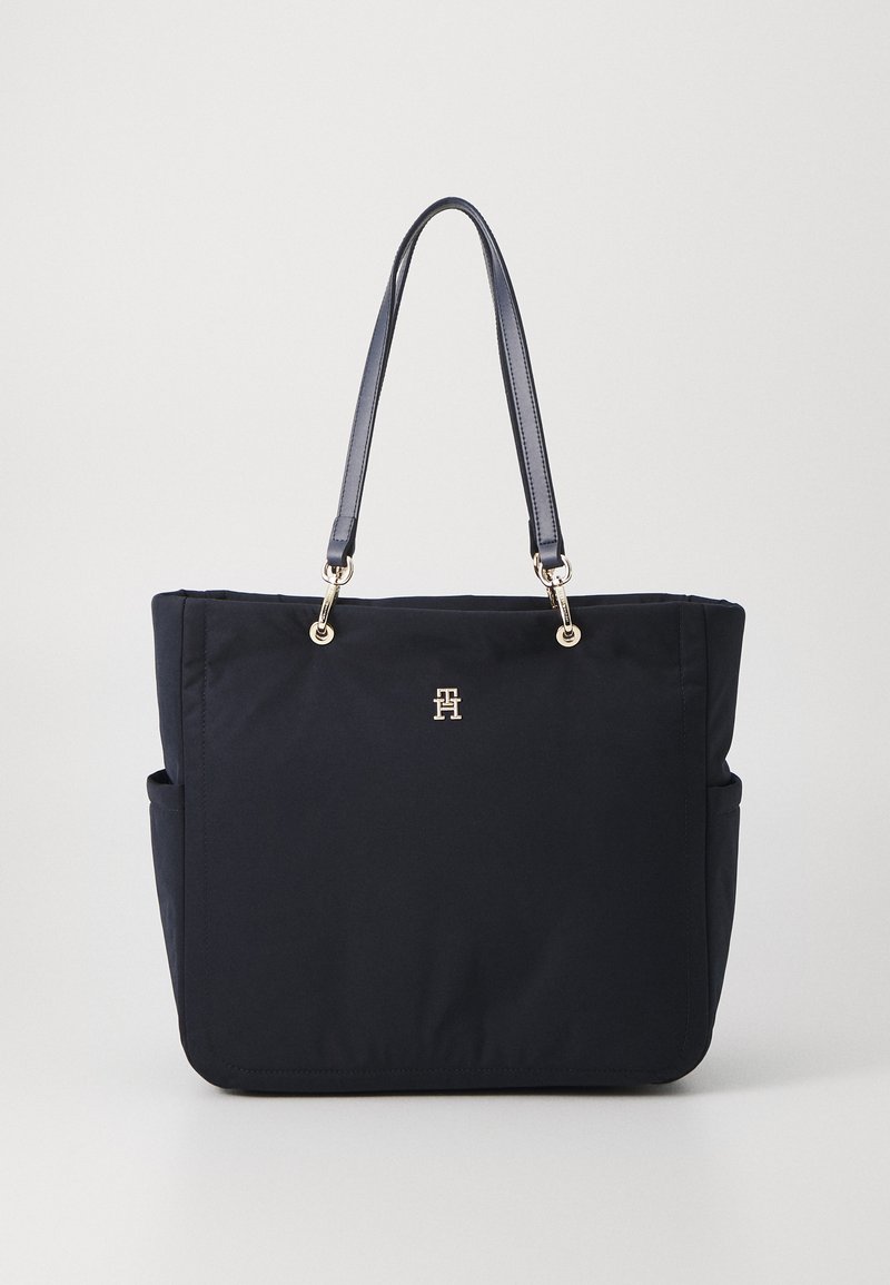 Navy tote bag made of durable fabric with two shoulder straps, gold-tone hardware, and a front logo detail. Features side pockets.