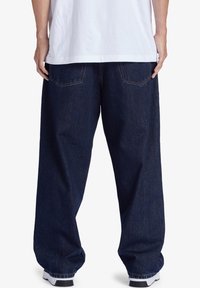 Tmavě modré džínové kalhoty s volným střihem a širokými nohavicemi, se dvěma zadními kapsami a kontrastním šitím. Nosit s bílým tričkem.