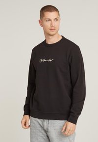 Black sweatshirt made of cotton blend, featuring a crew neck and long sleeves, with a small white cursive logo on the chest.