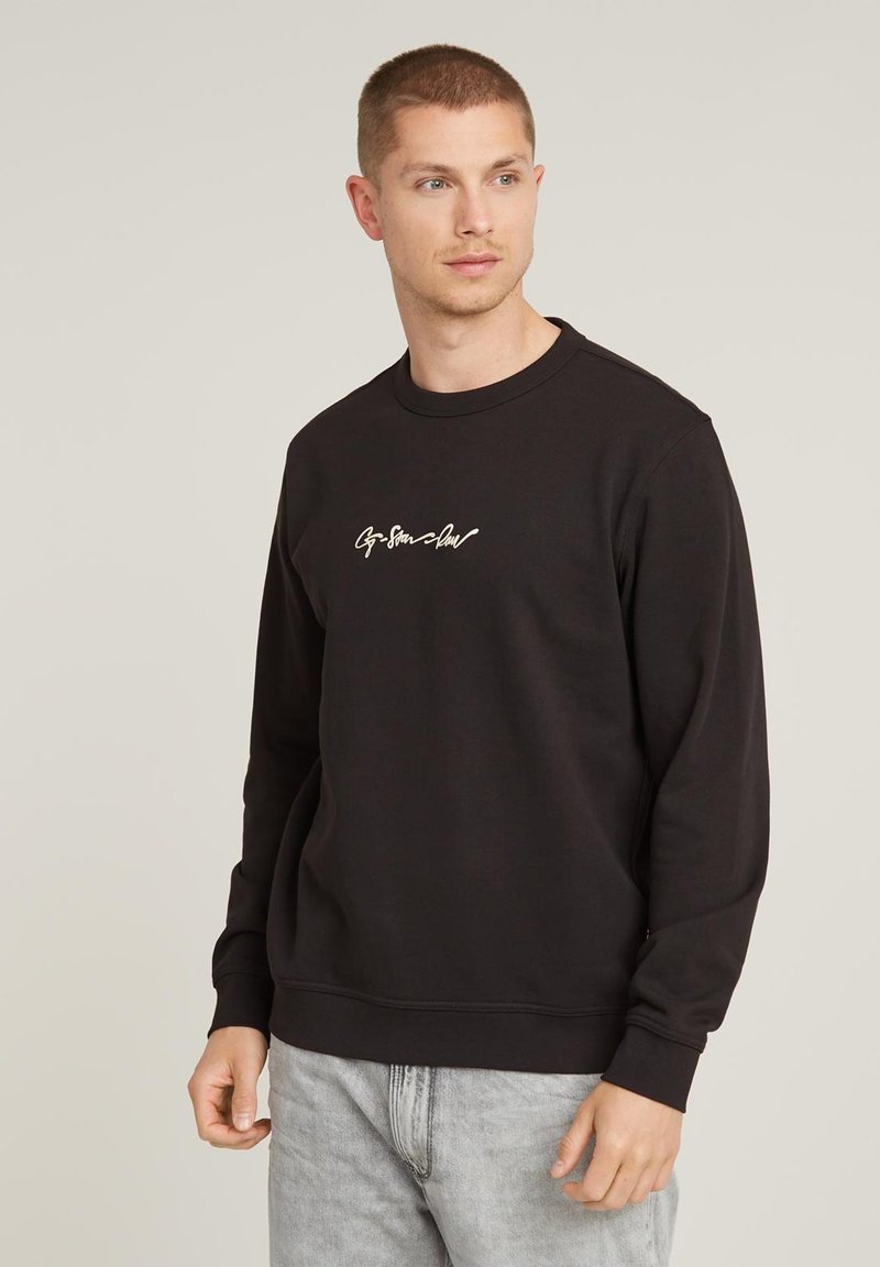 Black sweatshirt made of cotton blend, featuring a crew neck and long sleeves, with a small white cursive logo on the chest.