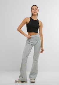 Top corto nero abbinato a pantaloni a campana fitted grigi chiari. I pantaloni presentano una vita ampia e una texture liscia. Sneakers grigie chiare.