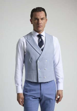 Chaleco de doble botonadura en azul claro con una tela texturizada, complementado con una camisa de vestir blanca y una corbata a rayas en azul marino. Ajuste entallado.