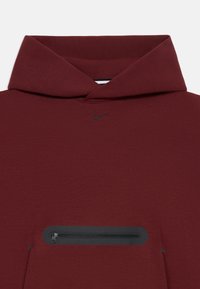 Bordová mikina s kapucňou s čiernym logom Nike swoosh pod výstrihom a horizontálnym čiernym zipsovým vreckom na prednej klokanke.