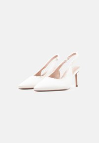 Escarpins à bride arrière blancs avec un design à bout pointu, un tissu texturé et des bords festonnés. Caractérisés par un talon fin et une doublure intérieure beige.
