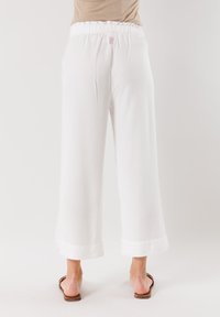 Pantaloni bianchi a gamba larga con elastico in vita, caratterizzati da orli arrotolati e una superficie liscia. Indossati con sandali marroni.