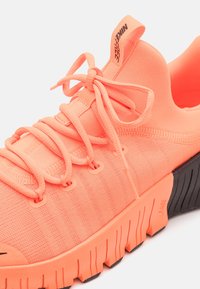Chaussure de course Nike Free corail vif avec dessus en tissu texturé, lacets attachés et semelle épaisse segmentée avec des accents noirs sur la bande de roulement.