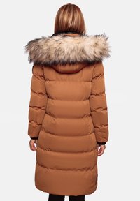 Lange bruine pufferjas met een volumineuze met bont gevoerde capuchon, verticale quiltpatronen en zwarte accenten. Ontworpen voor warmte en comfort.