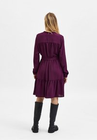 Lila långärmad klänning med volangkjol, texturerad tyg och bälte i midjan. Matchas med knähöga svarta stövlar.