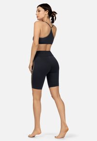 Czarny stanik sportowy z krzyżującym się dwuagam tyłem, w połączeniu z czarnymi szortami rowerowymi o wysokim stanie z bocznymi akcentami. Gładka faktura, dopasowany krój.
