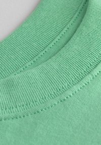 Détail de col en coton vert menthe avec un revêtement texturé et des coutures. Design incurvé, finition lisse et lignes de couture visibles.