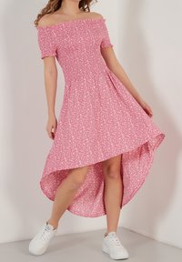 Vaaleanpunainen olkaimeton mekko, jossa on kukkakuosi, istuva vartalo ja korkea-alaspäin levenevä helma. Yhdistetty valkoisiin lenkkareihin.