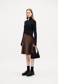 Maglione nero con zip, gonna in velluto a coste marrone con strisce verticali, borsa nera, mocassini spessi e calze nere. Texture liscia e look a strati.
