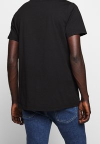 T-shirt in cotone nero con maniche corte, caratterizzato da un orlo dritto e una vestibilità classica, indossato con jeans in denim blu.